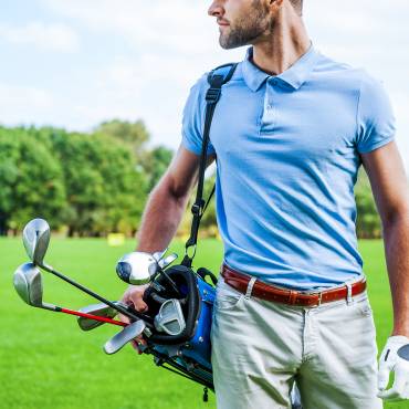 Golf is a style of living. Cropped image of male golfer carrying golf bag with drivers while walking by green grass